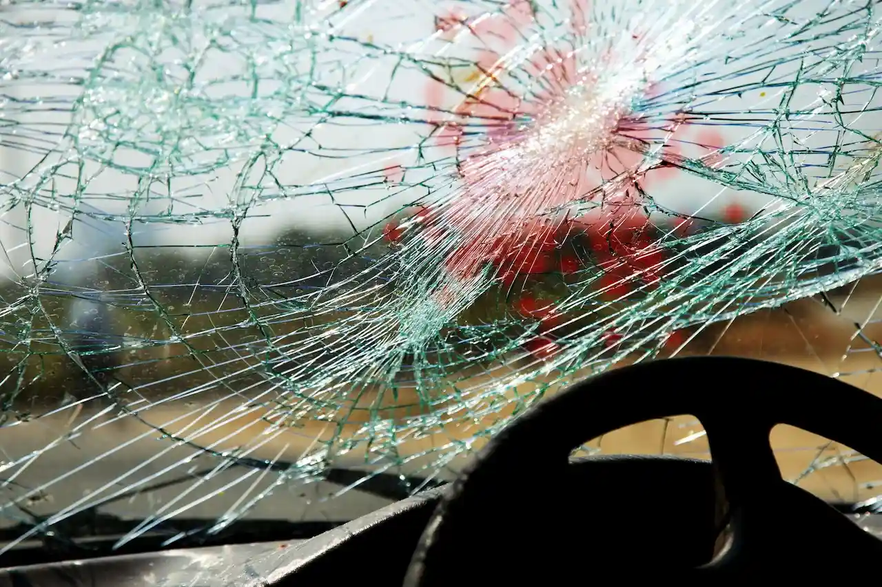 Shattered car windshield with spiderweb cracks radiating from a central impact point.